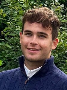 Junger Mann lächelnd im Garten mit blauem Pullover