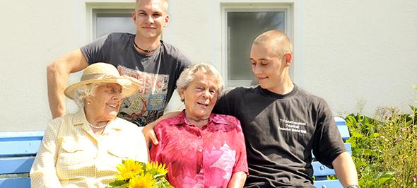 Zwei junge Freiwillige sitzen mit zwei Seniorinnen auf einer Bank